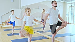 Tween girl with brother sitting on mat in modern yoga studio during family workout, doing exercises in pair