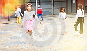 Tween girl in pink skirt jumping rope in schoolyard during recess