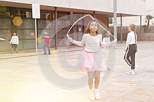 Tween girl in pink skirt jumping rope in schoolyard during recess