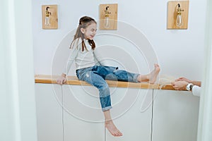 Tween girl sitting on a corridor shelf, her feet being tickled by her mom