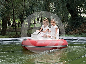 Tween girls riding on red inflatable motorboat in fun park