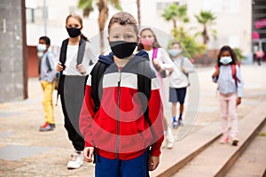 Tweenager in protective mask walking to school campus after lessons