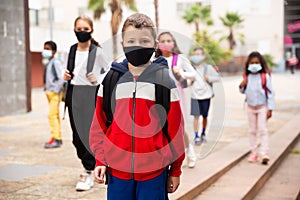 Tweenager in protective mask walking to school campus after lessons photo