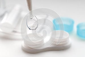 Tweezers with contact lens and plastic container on white background