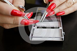 tweezers for eyelash extension in women& x27;s hands with a bright red manicure