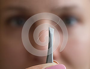 Tweezers with gray hair in front of the woman face