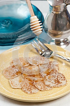 Twelve freshly prepared Jonny cakes, on a yellow plate, an artesen fork and honey being drizzled over the top