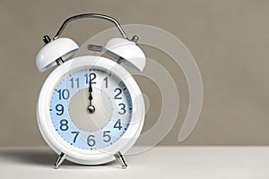 Twelve o'clock on the alarm. A white alarm clock is on a white table. The clock hand points to 12 o'clock. Time