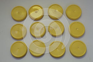 Twelve plastic yellow round lids for jars on a white background