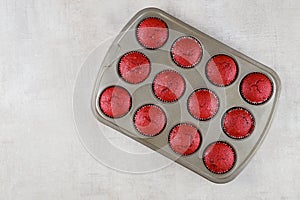 Twelve red velvet cupcakes in baking pan on white background