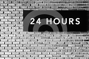 Twenty four hours glowing sign on brick wall, black and white s