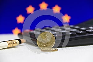 Twenty France euro cent on obverse on white floor with black calculator and pencil, European Union flag.