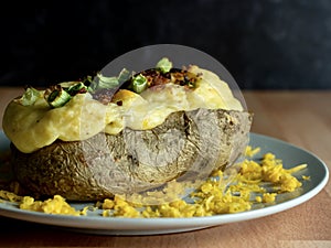 Twice Baked Potato Loaded with Scallions, Bacon and Cheddar Cheese Baked to Perfection on a Gray Plate Garnished with More Cheese