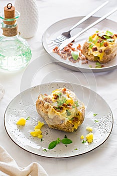 Twice-baked potatoes in their skins with cheese and bacon crumbs on plates on a wooden table. Flexitarian Diet. Vertical vew