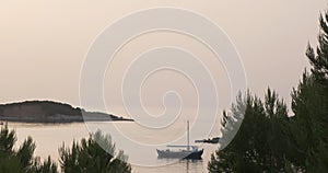 Twilight in a calm quiet sea bay. View of the trees and the island in the distance, the yacht on the water. Wide shot