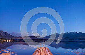 Twilight at lake Hopfensee in Bavaria with pier and mountains mirroring in water