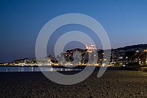 Twilight over a calm beach, city lights and a lit cathedral in the background, peaceful evening scene.