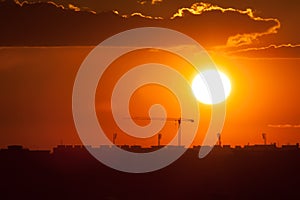 Twilight over the city of Bucharest. Construction crane, building silhouettes and sun circle in the background