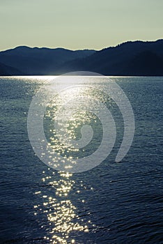 Twilight seascape. Mountains and sun glint in the water