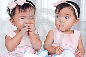 Twin babies in pink dress, one looking, one crying