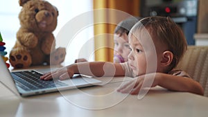 Twin baby children a playing laptop watching video in the kitchen. Happy family kid dream concept. Baby twins playing