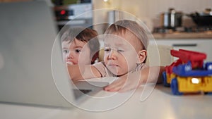twin baby children a playing laptop watching video in the kitchen. happy lifestyle family kid dream concept. baby twins