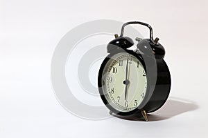 Twin bell alarm clock black color on six o`clock put on the white floor