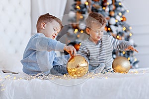 Twin brothers in front of the christmas tree with candles and gifts. love, happiness and big family concept