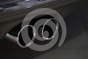 Twin chrome tailpipe of powerful sports car with black body and gray plastic parts