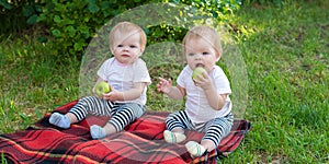 Twin girls in the city park sitting on blanket