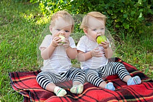 Twin girls in the city park sitting on a blanket