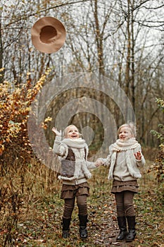 Twin girls play in the autumn park, throw their hats up