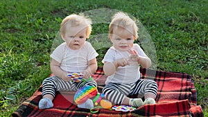 Twin girls play with bright toys on a blanket in a city