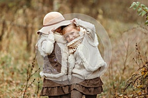 Twin girls play with a hat in the autumn park