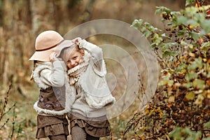 Twin girls play with a hat in the autumn park