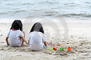 Twin girls while playing beach toys and sitting on a beach sand with white sand and waves