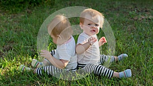 Twin girls are sitting on green grass with their backs