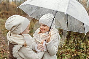 Twin girls stand under an umbrella in an autumn park, communicate, smile