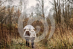Twin girls walk through the autumn park under an umbrella
