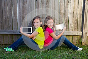 Twin sister girls playing tablet pc sitting on backyard lawn