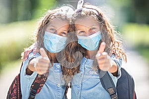 Twin sisters with face masks go back to school during the Covid-19 quarantine and showing thumbs up