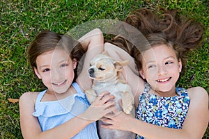 Twin sisters playing with chihuahua dog lying on lawn
