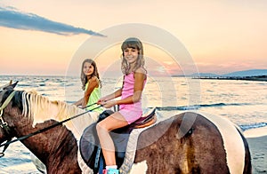 Twin sisters riding horses in the sunset by the sea on the isla