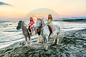 Twin sisters riding horses in the sunset by the sea on the isla