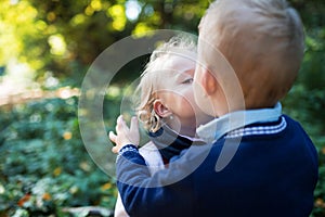 Twin toddler sibling boy and girl standing in autumn forest, kissing.