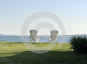 Twin white Adirondack chairs seaside in sunlight