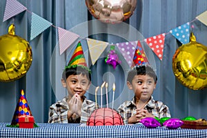Twins adorable boy in shirt, celebrating his birthday, blowing candles on homemade baked cake, indoor. Birthday party for kids