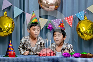 Twins adorable boy in shirt, celebrating his birthday, blowing candles on homemade baked cake, indoor. Birthday party for kids