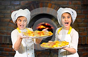 Twins. Beautiful sisters twins girls in cook hats holding pizza