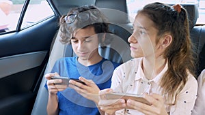 Twins brother and sister use the phone while traveling in the car